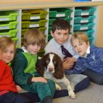 Four kids sat in front of green trays, stroking a brown and white dog.