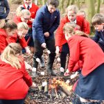 Kids in red blazers and navy coats stood around a campfire with marshmallows on sticks