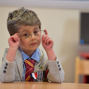 A young school boy dressed up as an old man with glasses, wearing a suit and tie.