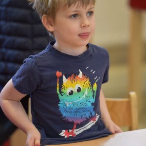 A young boy wearing a t-shirt that has a multi-coloured monster riding a skateboard.