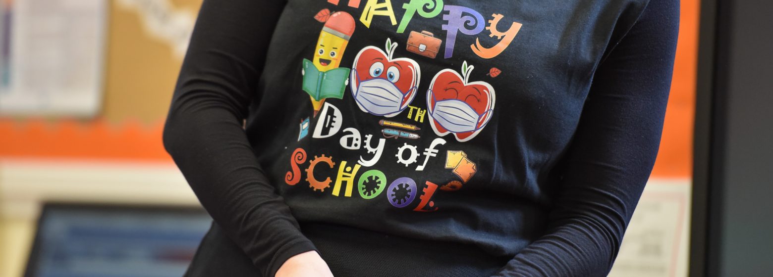 A teacher wearing a t-shirt that says 'Happy Day of School'