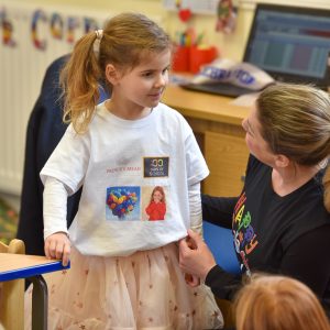 A child and her teacher in a gclass room talking to each other, both with ponytails.