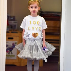 A young red haired girl dressed as a princess, with a gold tiara and tutu.