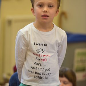 A boy in a school hall wearing a white t-shirt and green shorts.