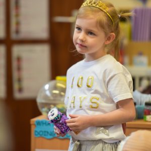 A young blonde girl holding a plush owl toy, and wearing a white t-shirt.