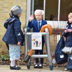 Three kids stood outside school, dressed up as older verisons of themselves.