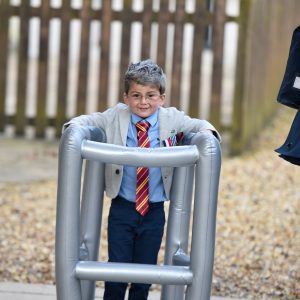A small child dressed up as an old man, walking with an inflatable zimmer frame.