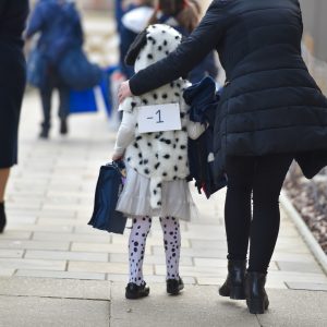 A small school child dressed as a Dalmatian walking on a pavement with her mother.