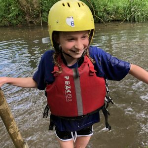 Child exiting a river wearing a helmet and an inflatable jacket